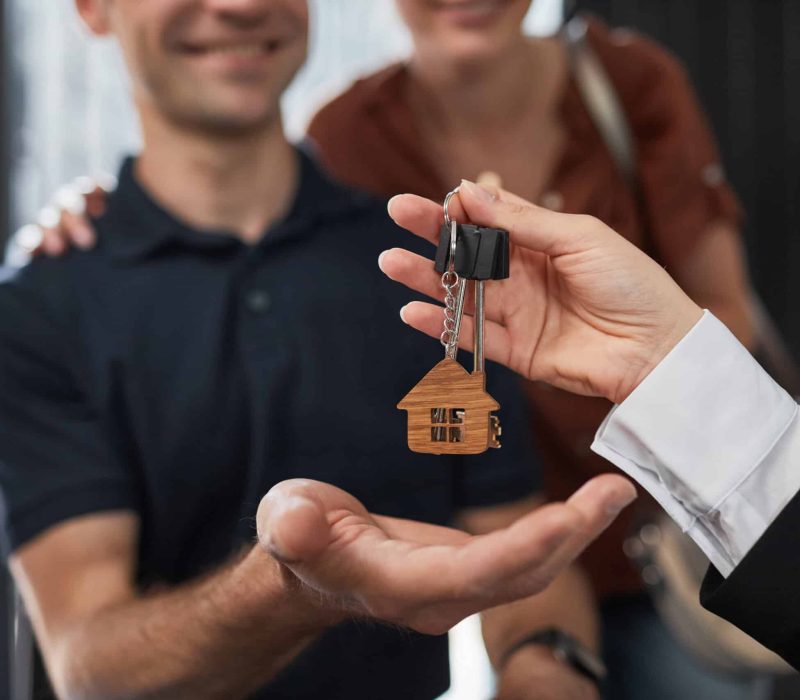 Close up of real estate agent giving keys to couple with focus on house keychain, copy space